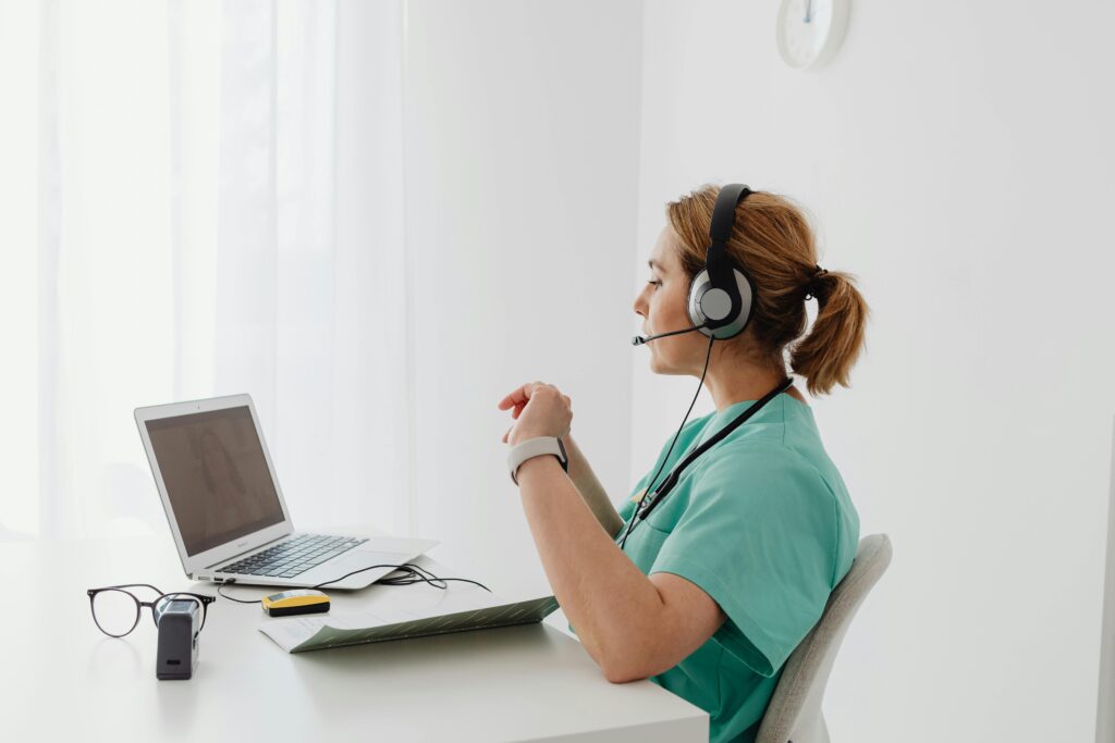 Sobre nosotros 1 A female doctor using a laptop for an online consultation, wearing a headset in a bright office.